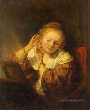 Jeune femme essayant des boucles d’oreilles Rembrandt Peinture à l'huile